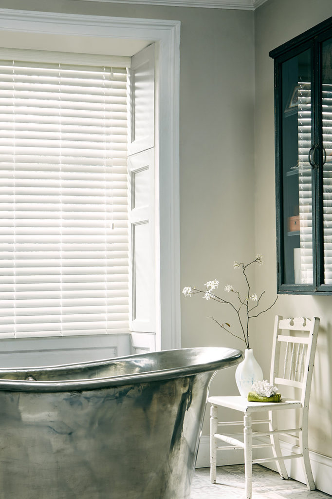 White faux wood venetian blinds in bathroom with metal bathtub.