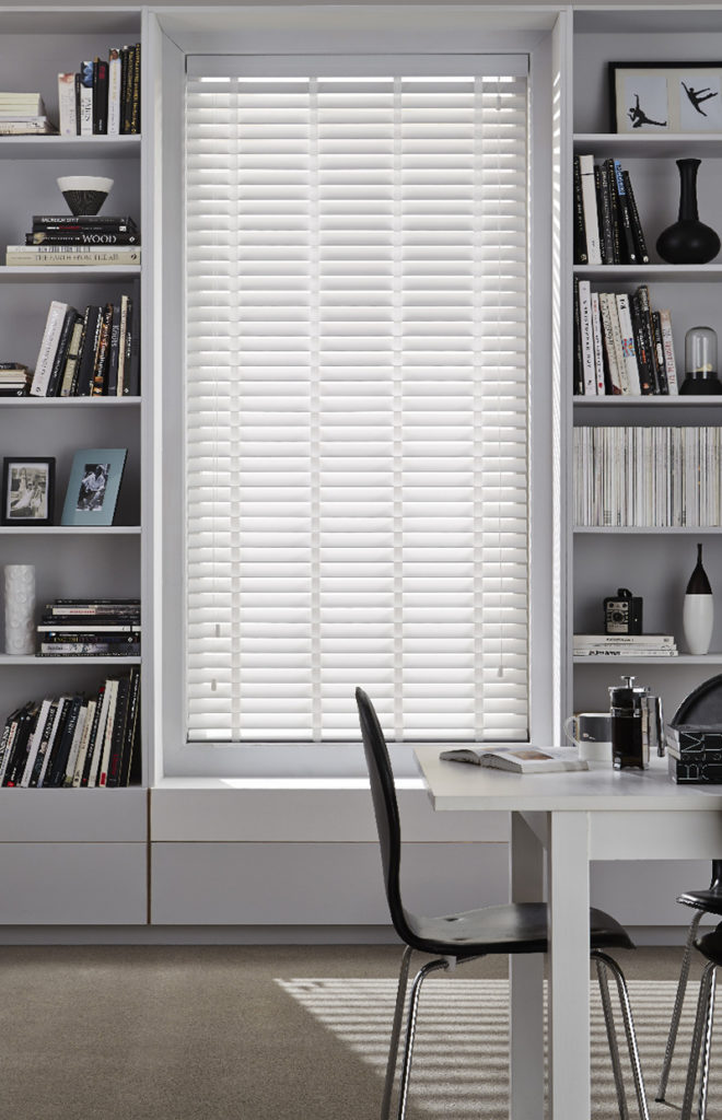 White wooden venetian blinds in living room with bookcase.