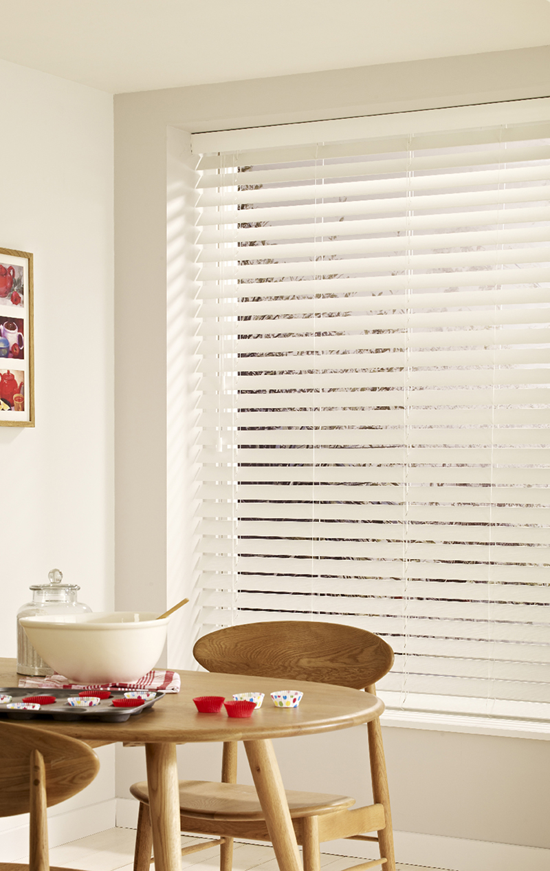 image of wooden table next to window with white wooden blinds 