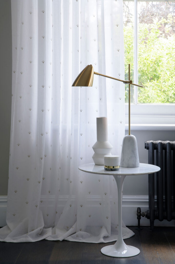 Gold lamp shade next to white voile curtain.