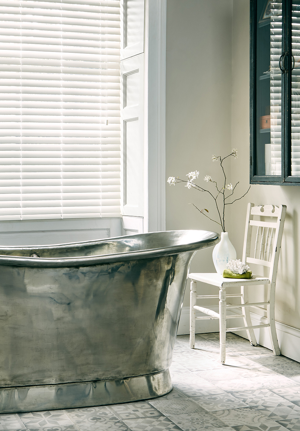 photo of stand alone bath next to window with white faux wooden blinds 