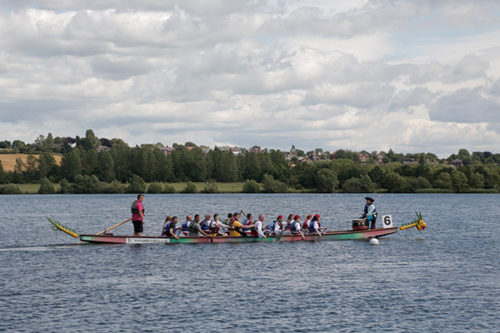 photo of narrow rowing boat on the river with people rowing it 