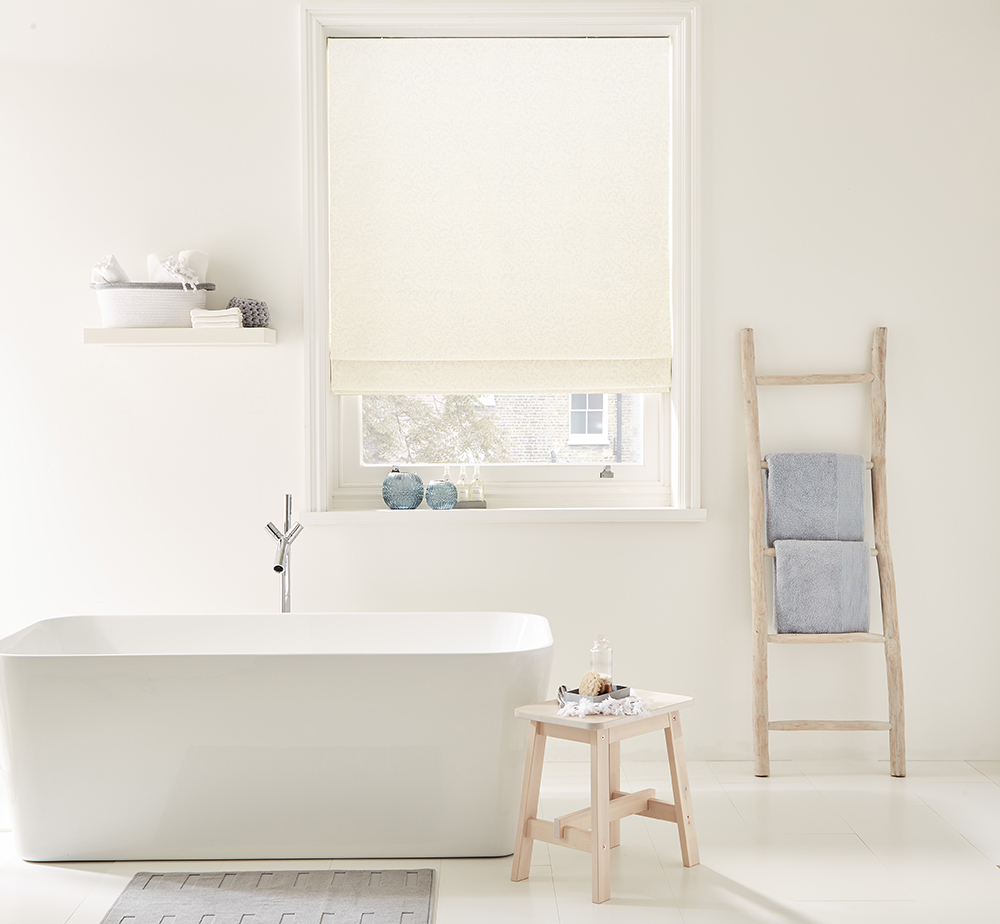 image of white bathroom with stand alone white tub next to window with white roller blinds 