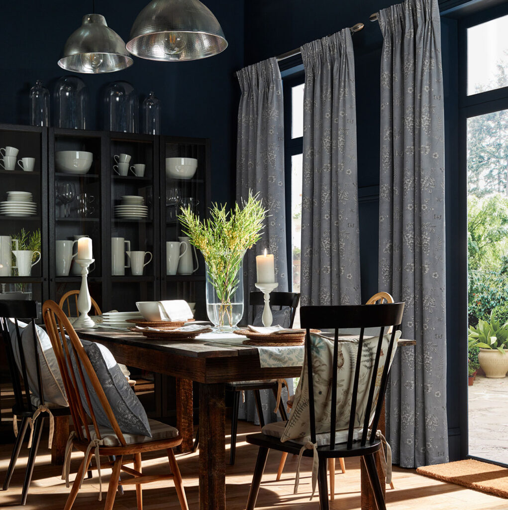 dark blue wall with light grey curtains in dining room with candles and 4 brown chairs