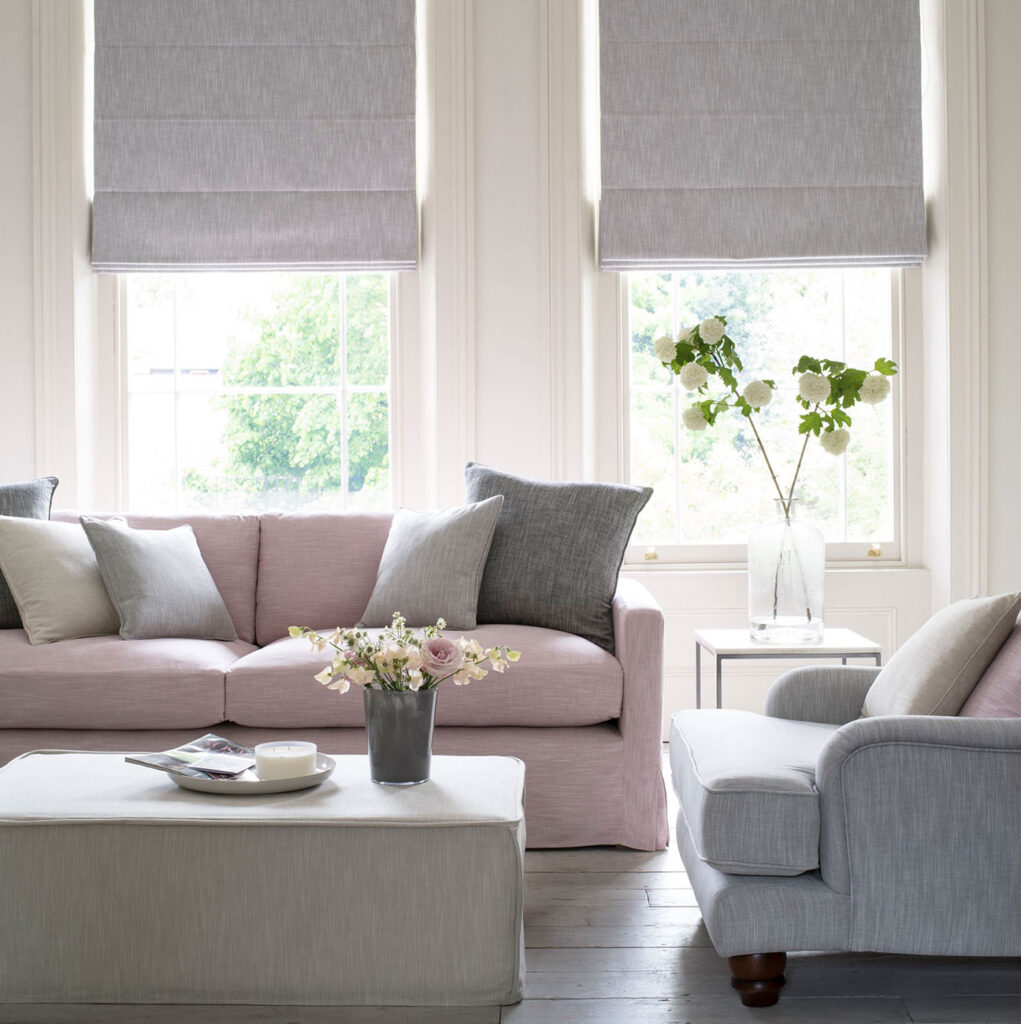 living room with grey roman blinds and a pick sofa with cushions and flowers