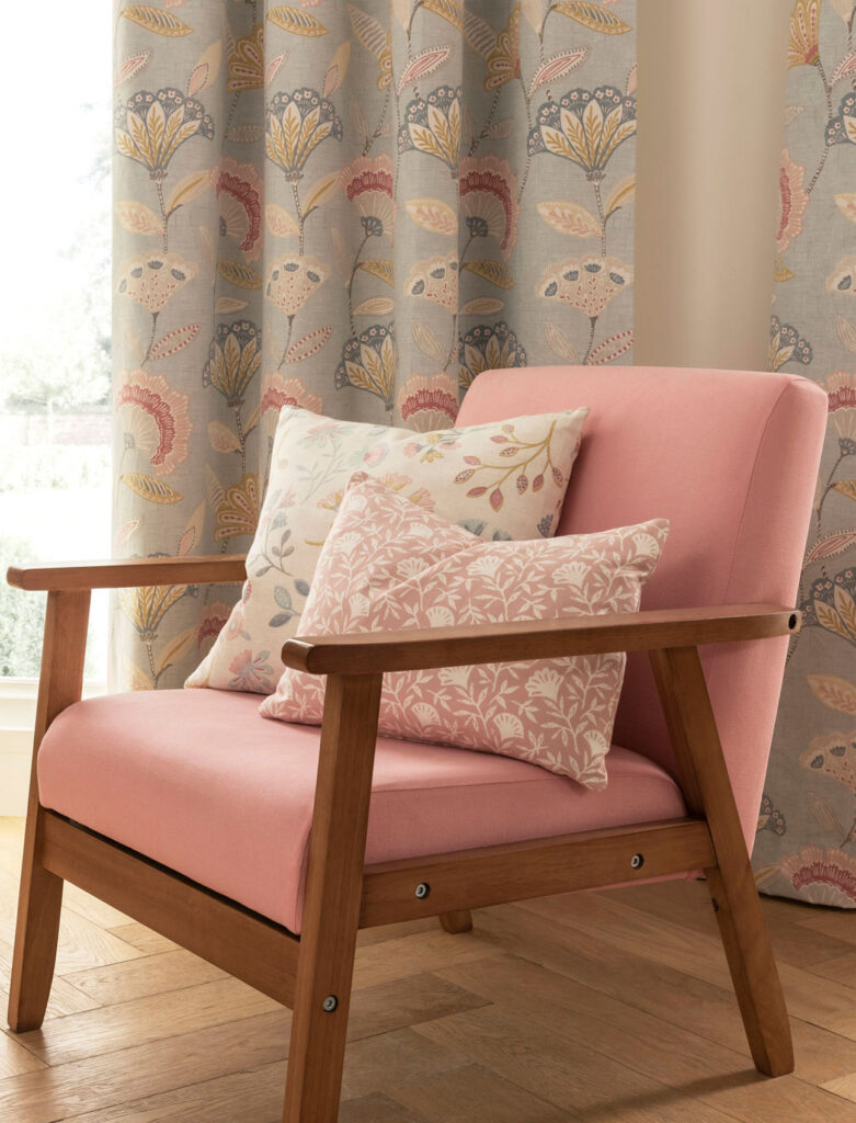 pink chair with with two floral print cushions next to light blue curtain