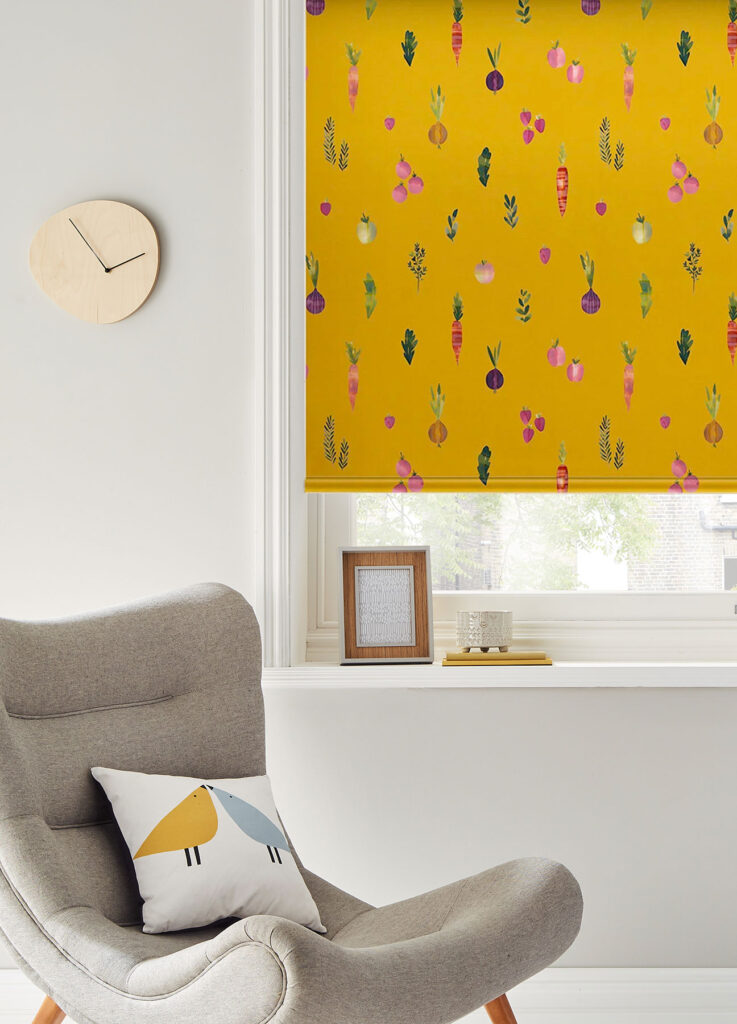 yellow roller blind with fruit and vegetable design on it next to grey chair with animal print cushion 