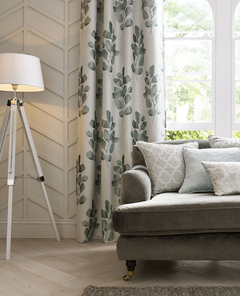 photo of white curtains with eucalyptus colour print in living room next to grey sofa with cushions 