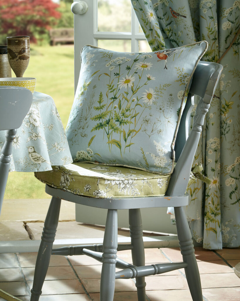 close up image of baby blue painted wooden chair with cushion on top next to open window 