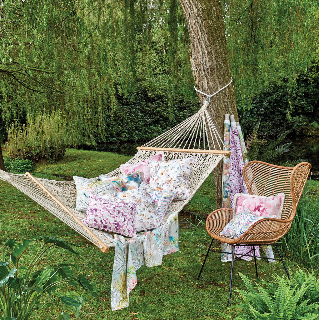 photo of garden with hammock tied to tree with cushions on top next to wicker chair 