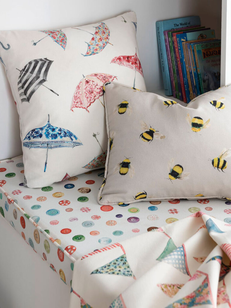 image of two cushions with umbrella and bumble bee printed design resting next to books 