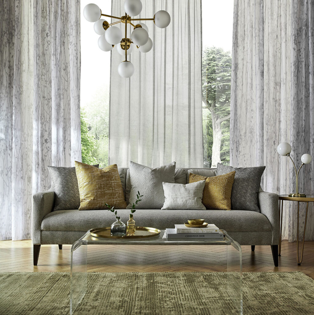 room set image of soft green sofa in front of a floor to ceiling window with linen curtains 