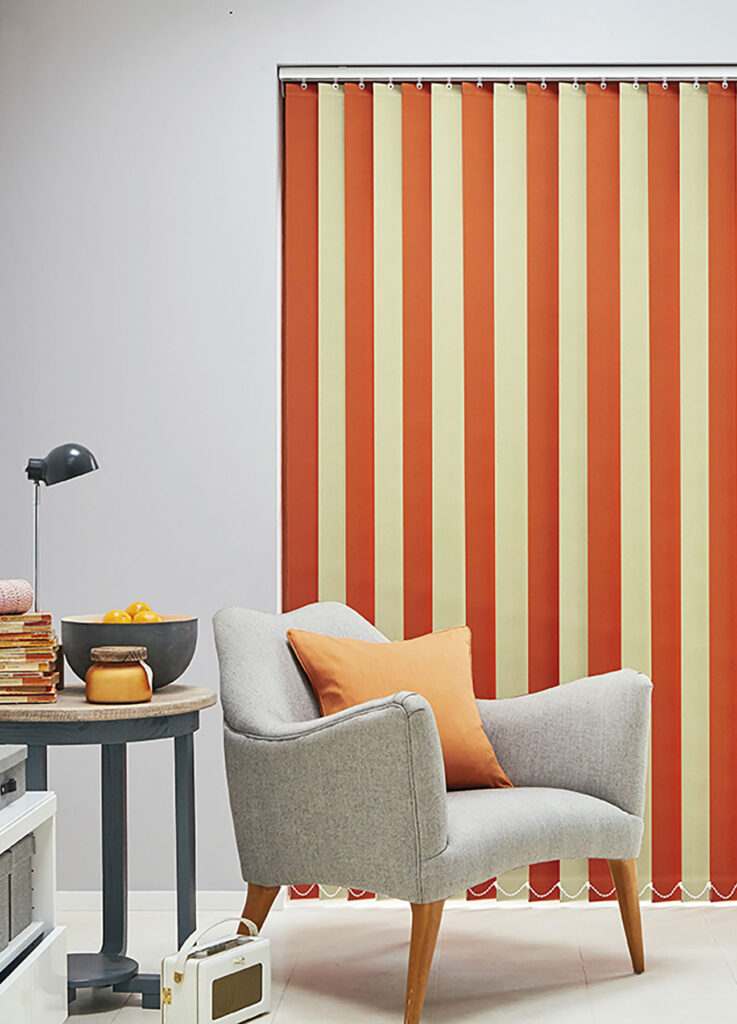 photo of chair next to window with closed orange and cream alternate vertical blinds 