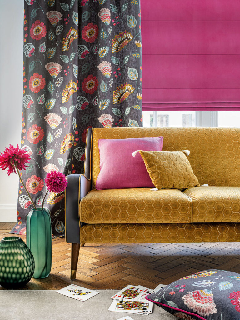 image of sofa next to window with bright pink roman blind and floral curtain