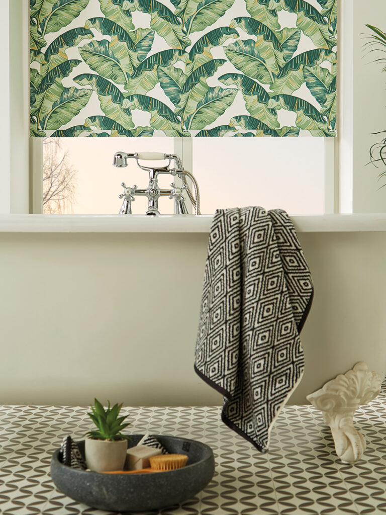close up image of cream bath tub next to window with green leaf print blind