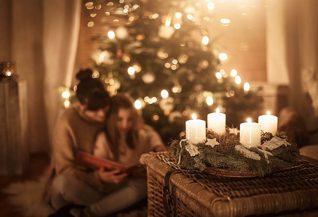 a photo of two girls sat in  a candle lit living room next to Christmas tree reading a book