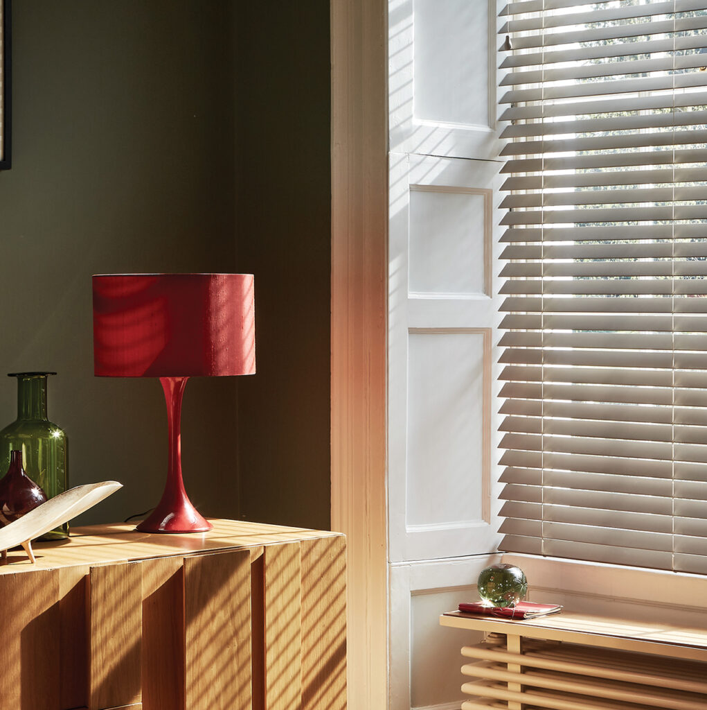 image of large window dressed with bamboo venetian blinds with red lamp in front of it 