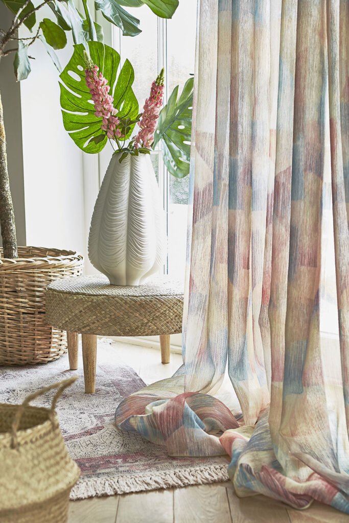 close up image of colourful sheer curtains hanging next to a house plant 