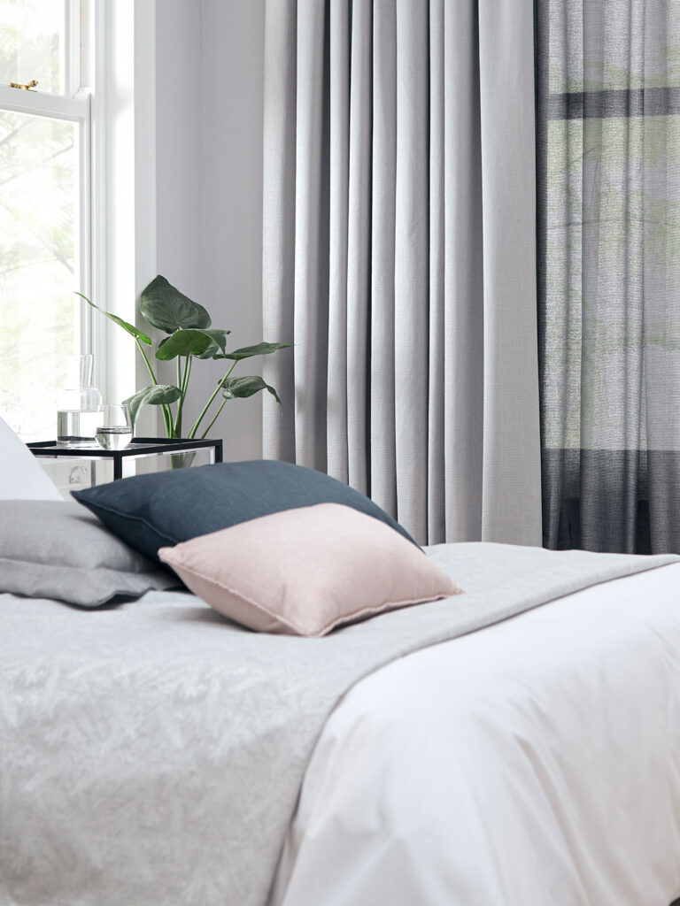 image of a bed with cushions on top of it next to a window and sheer curtains