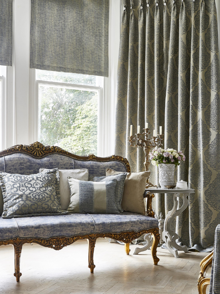 A neoclassical window space with curtains, cushions, roman blinds and an ornate sofa.