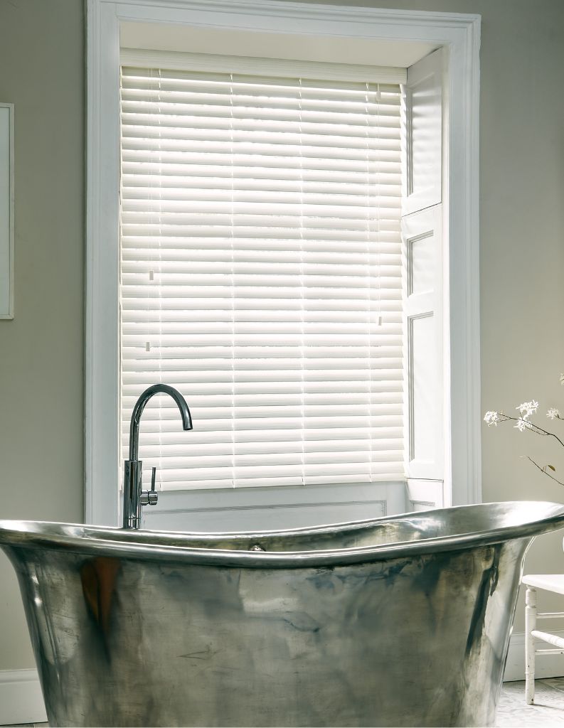 A stylish spathroom featuring a classic metal bathtub and faux wooden blinds.