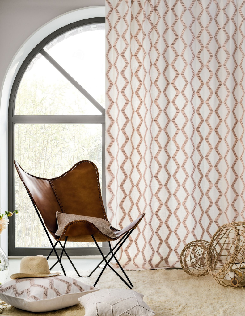 A retro 70s inspired sitting room featuring patterned curtains and a slim leather arm chair.