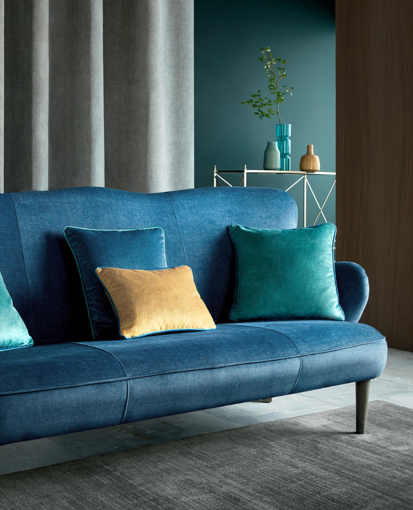 Velvet cushions on a shiny sofa with soothing grey curtains at the windows. 