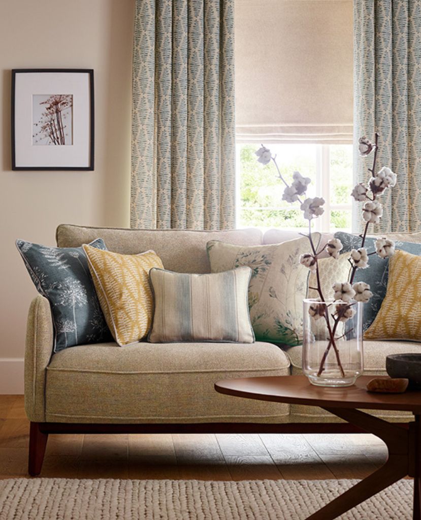 A cosy living room featuring patterned curtains, different styles of cushion and a textured rug in front of the sofa. 