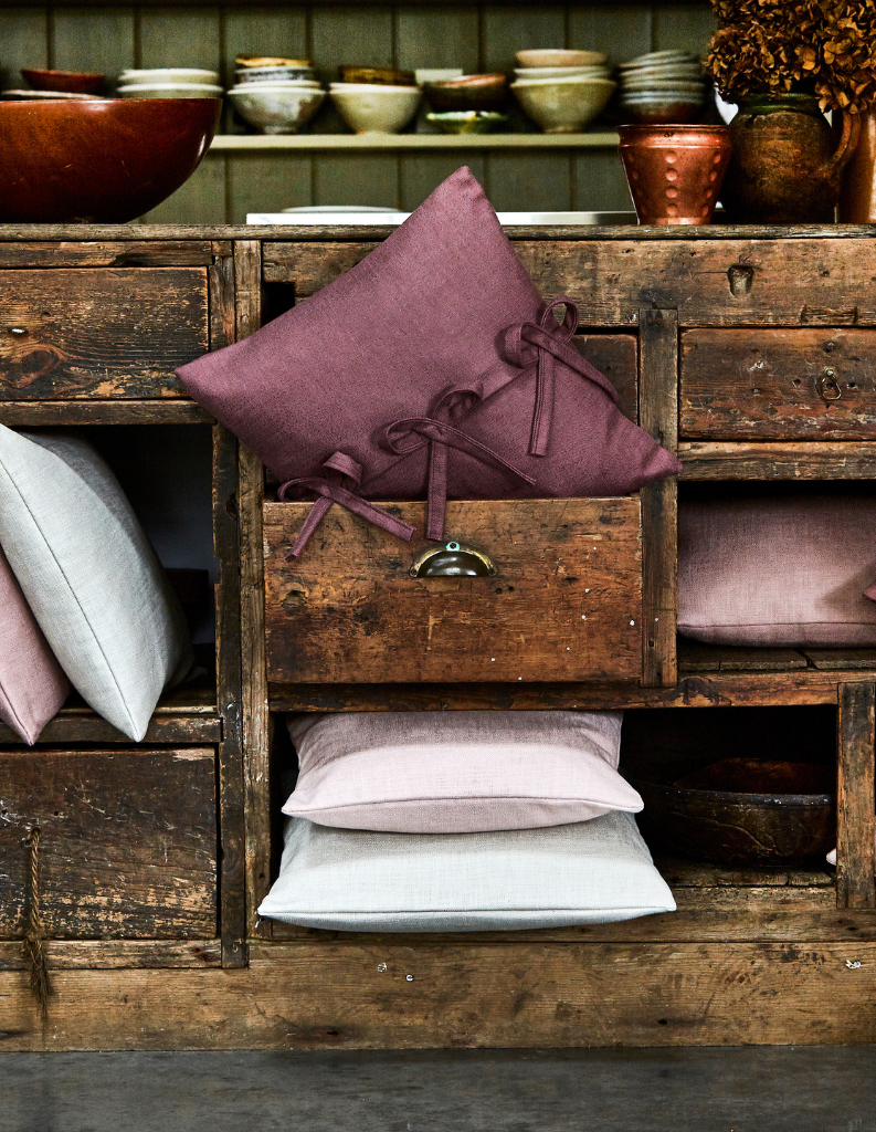 A country side cabinet with purple, pink and white cushions. 